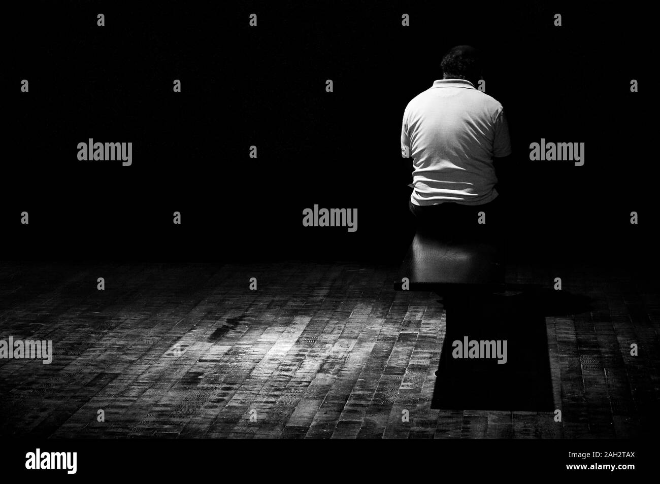 Un homme seul est assis sur un banc dans l'obscurité, avec son dos vers l'appareil photo Banque D'Images
