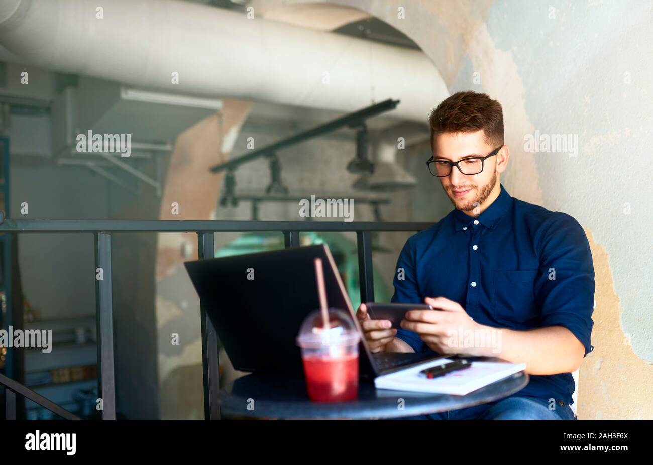 Handsome businessman distraite de travailler sur l'ordinateur portable regardant la vidéo sur smartphone. Freelancer holding mobile phone et l'aide de navigation 4g haute vitesse Banque D'Images