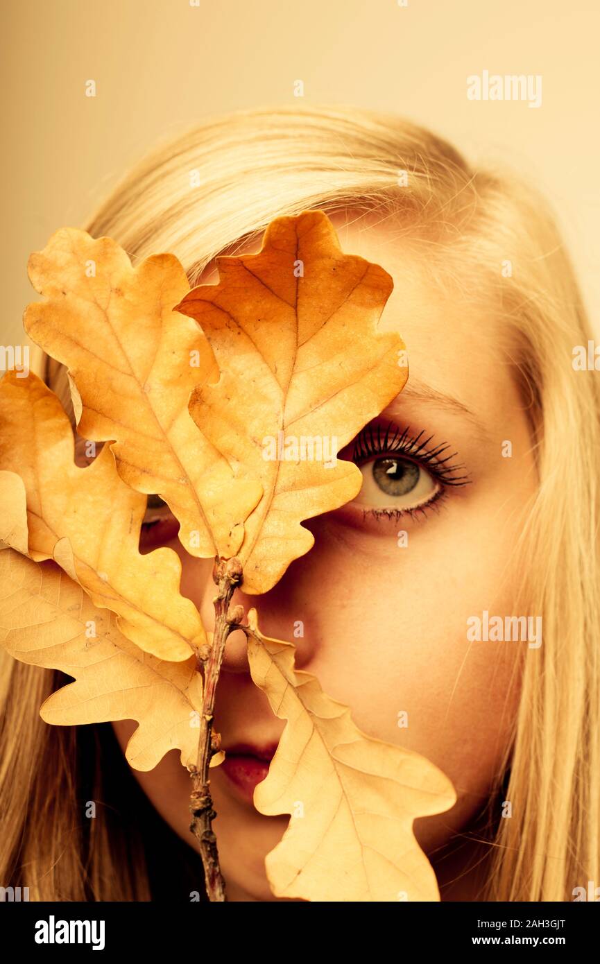 Jeune femme blonde derrière une branche d'acorn laves en couleurs automnales Banque D'Images