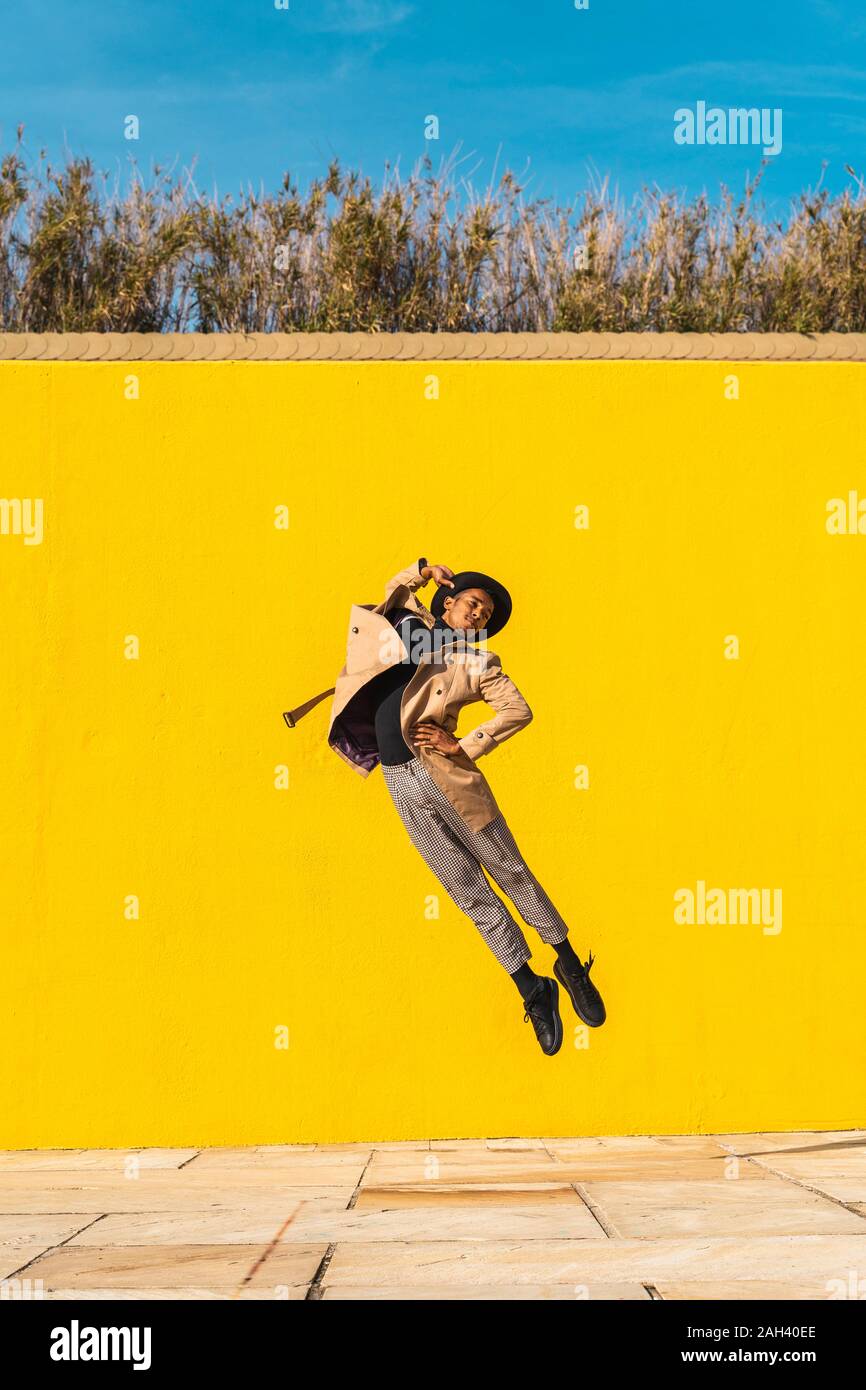 Jeune homme danser devant mur jaune, jumping mid air Banque D'Images