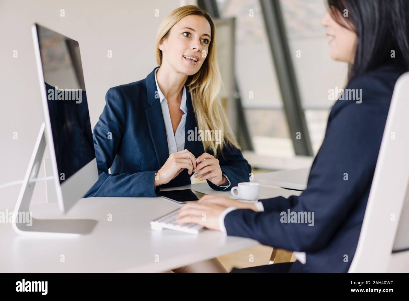 Two businesswomen sitting at desk in office talking Banque D'Images