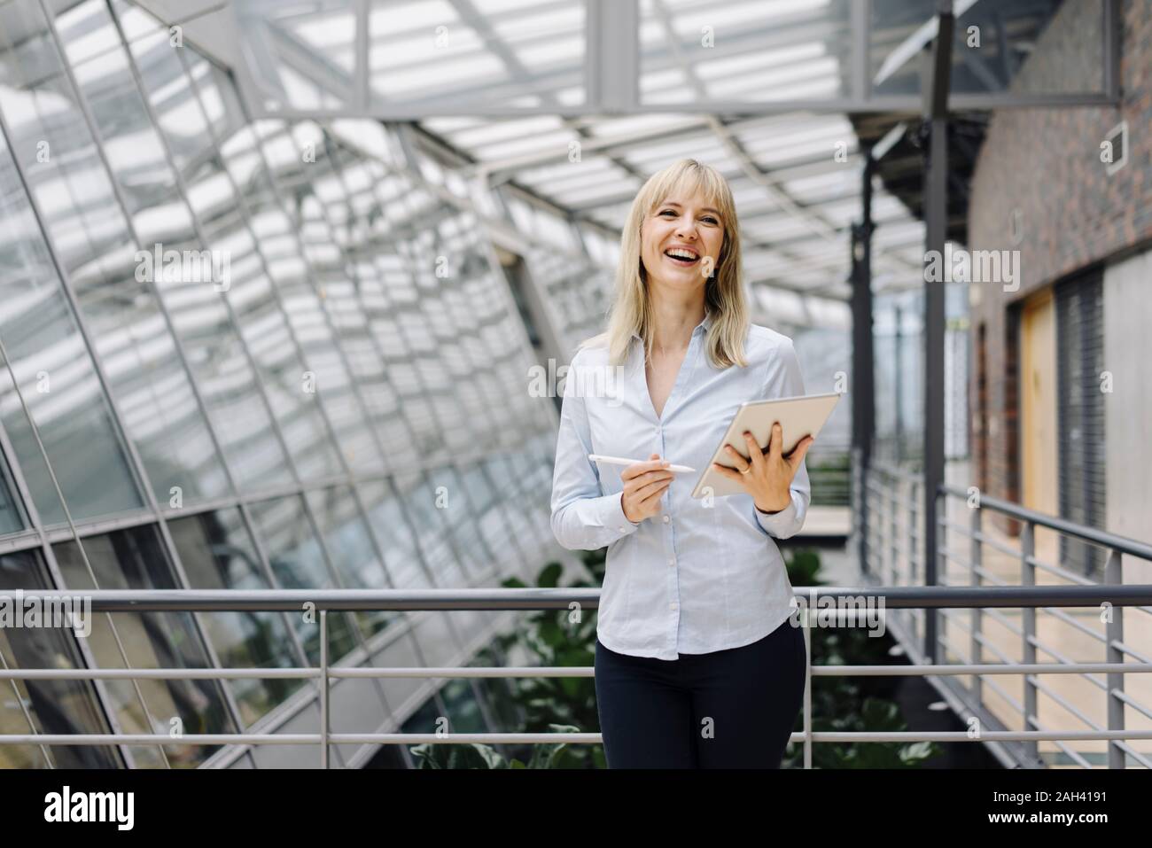 Laughing young businesswoman in a modern office building using tablet Banque D'Images
