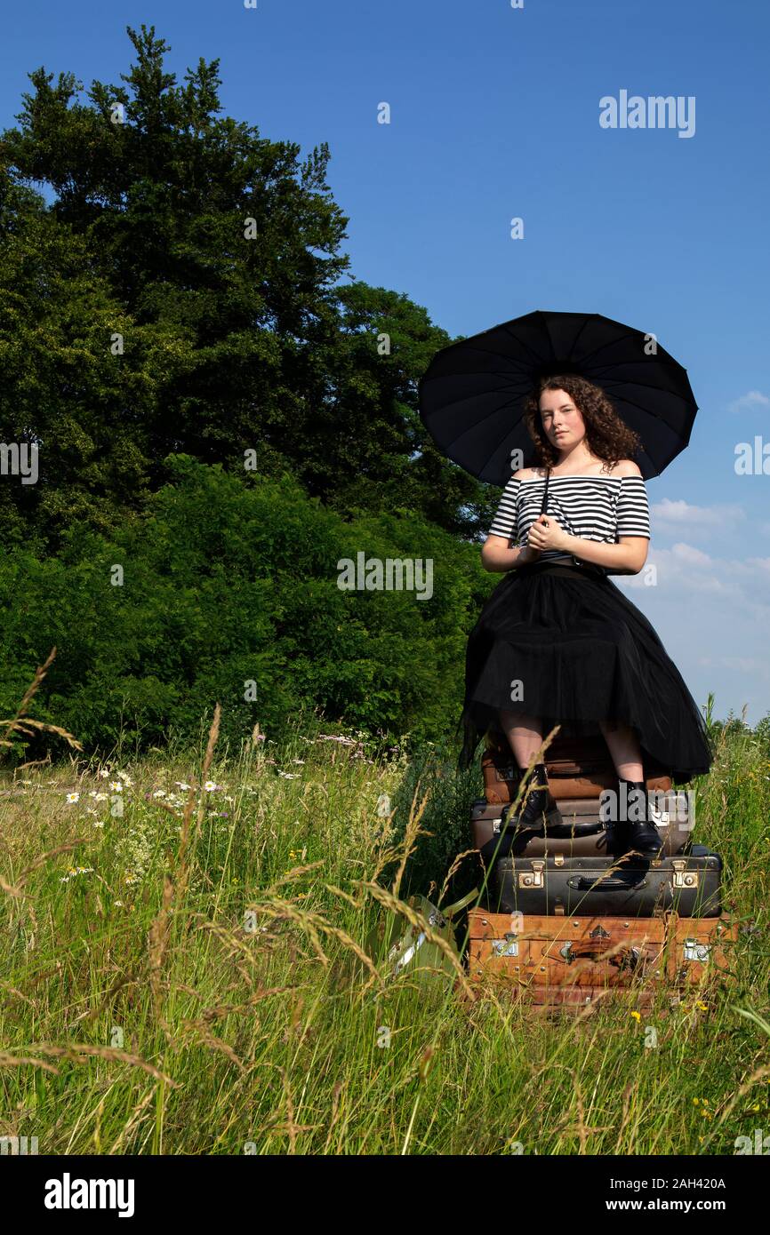Portrait de jeune femme avec parapluie assis sur de vieux valises sur un pré Banque D'Images