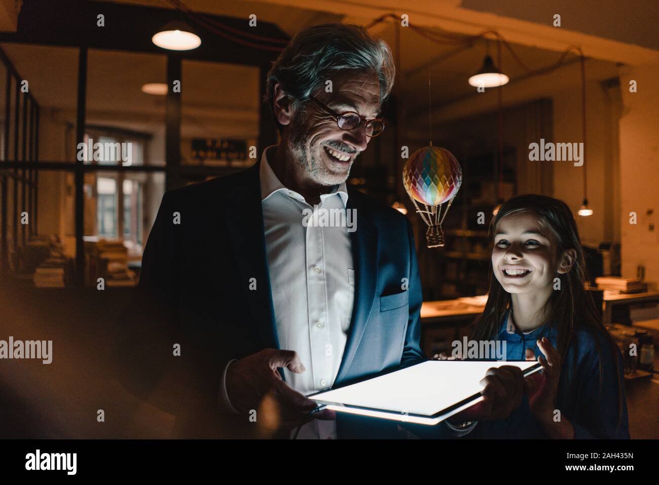 Happy senior buisinessman et fille avec ballon à air chaud et brillant tablet in office Banque D'Images