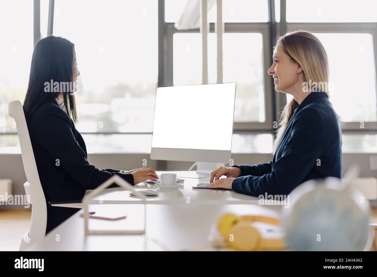 Two businesswomen sitting at desk in office talking Banque D'Images