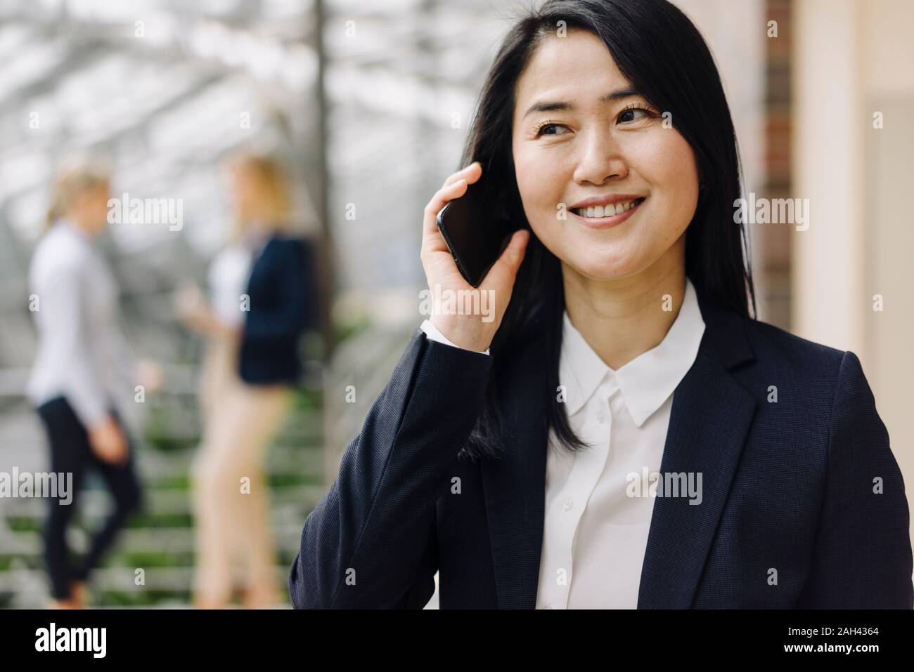 Portrait of a smiling businesswoman on the phone in office avec des collègues en arrière-plan Banque D'Images