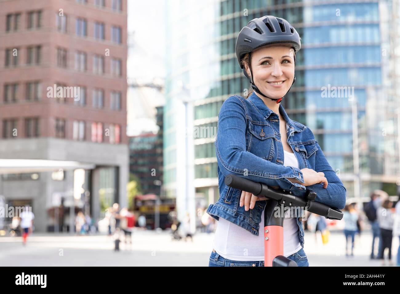 Portrait of smiling woman with e-scooter dans la ville, Berlin, Allemagne Banque D'Images