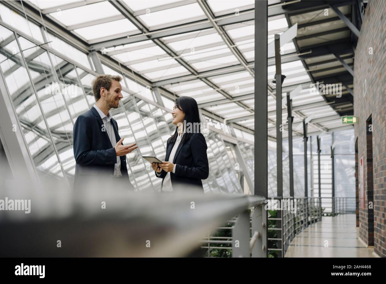Smiling businessman and businesswoman with tablet talking in modern office building Banque D'Images