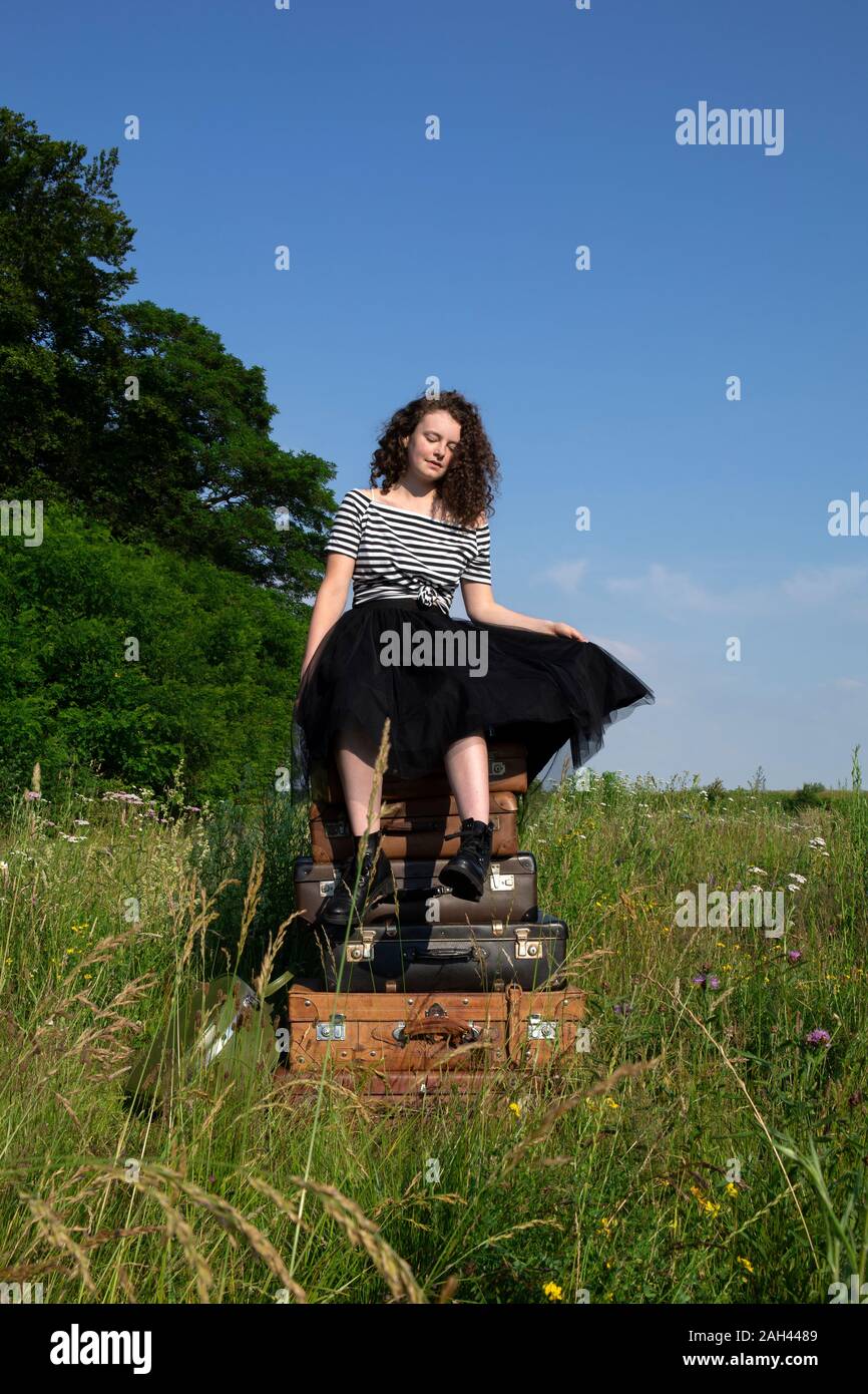 Portrait de jeune femme assise sur de vieux valises sur un pré Banque D'Images