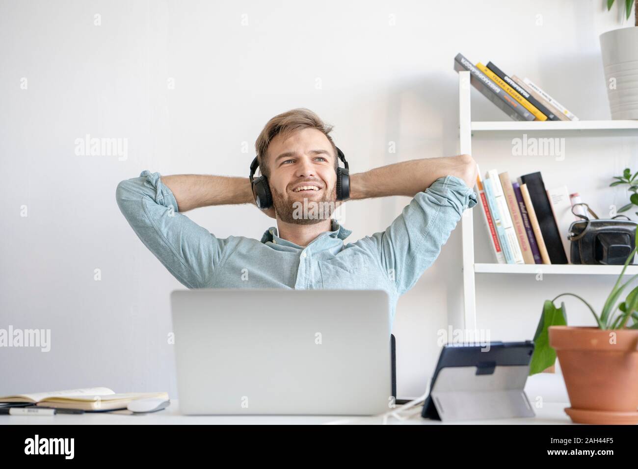 Smiling man listening to music at desk in office Banque D'Images