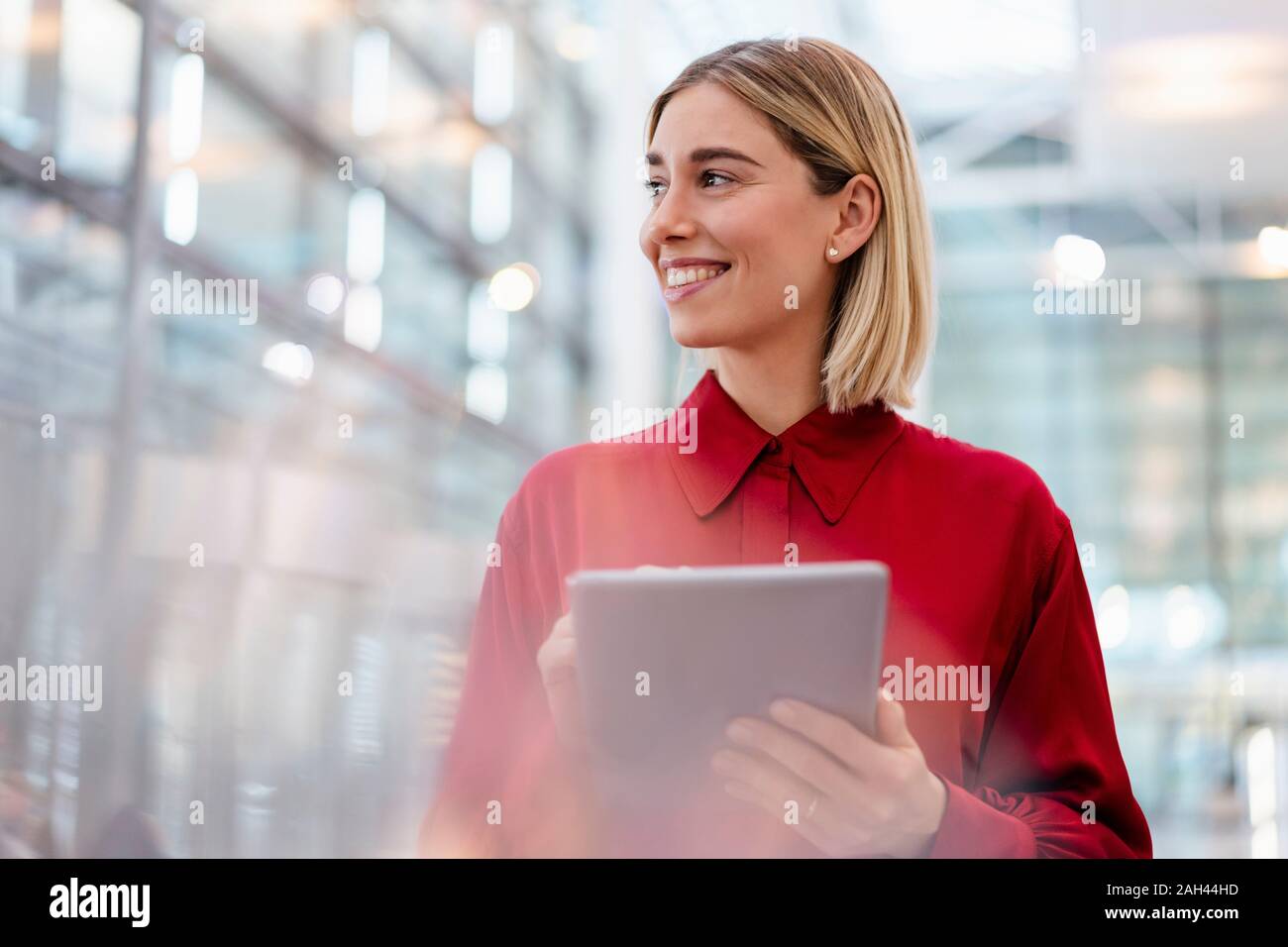 Smiling young woman wearing red shirt using tablet Banque D'Images