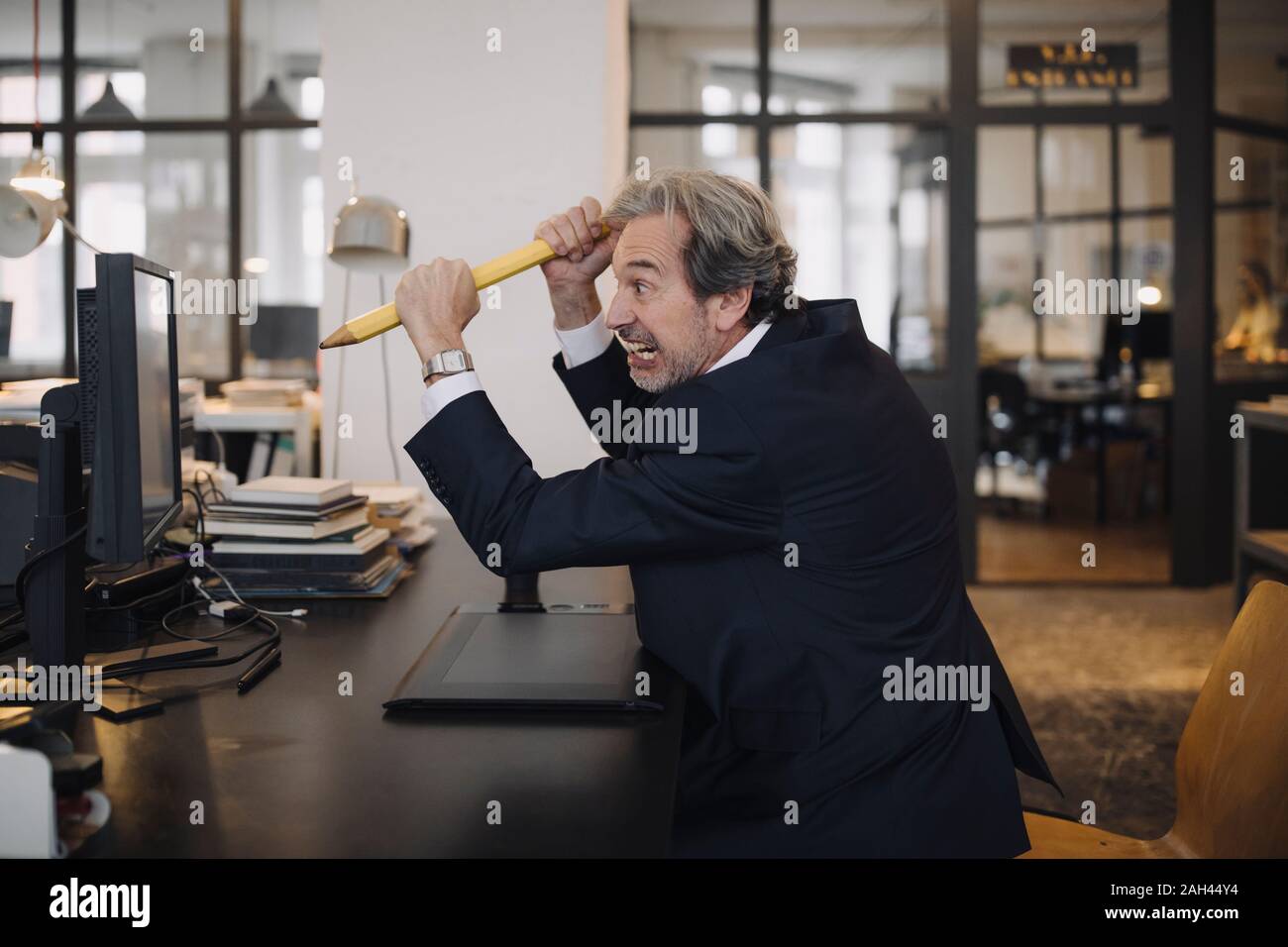 Angry senior businessman avec crayon géant at desk in office Banque D'Images