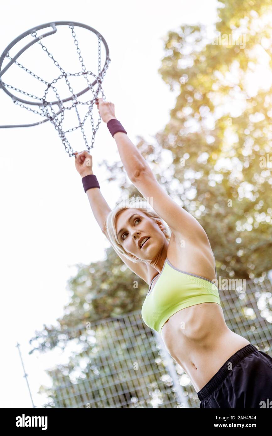 Femme blonde jouant au basket, hanging on hoop Banque D'Images