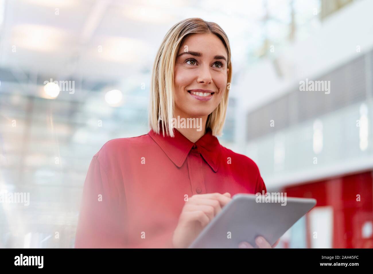 Smiling young woman wearing red shirt using tablet Banque D'Images