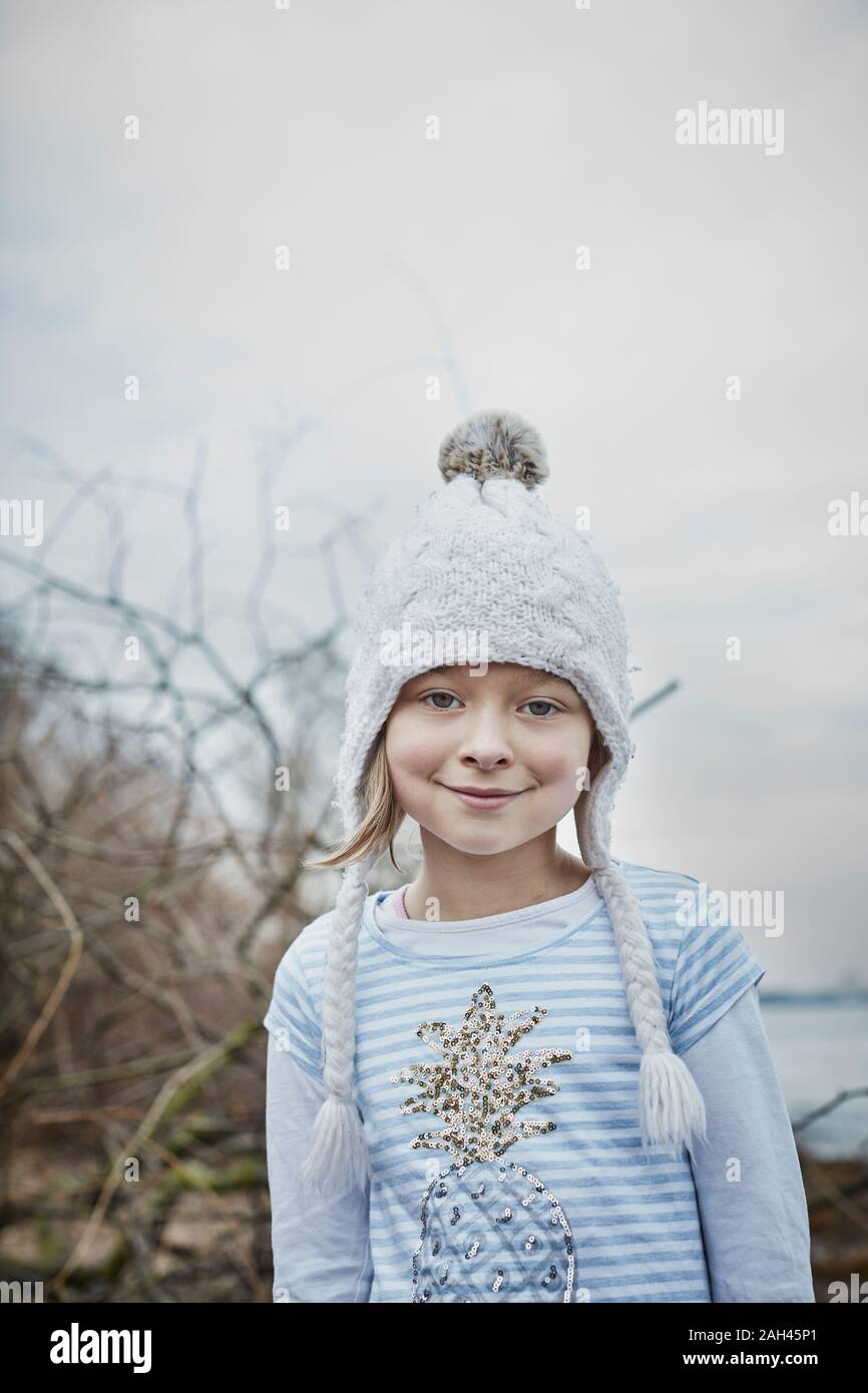 Portrait of smiling little girl wearing bobble hat dans la nature Banque D'Images