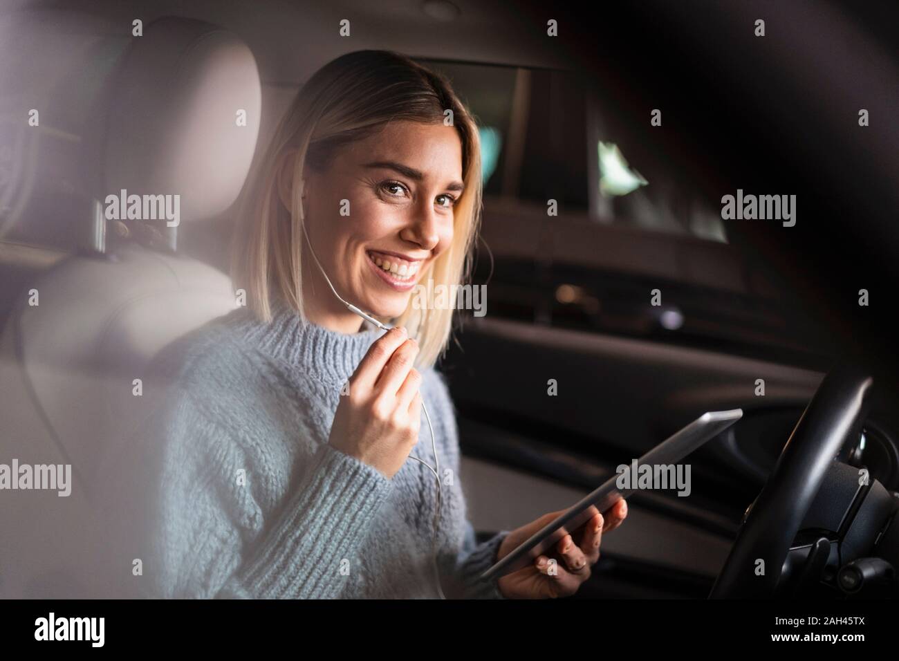 Happy young woman with tablet et écouteurs dans une voiture Banque D'Images