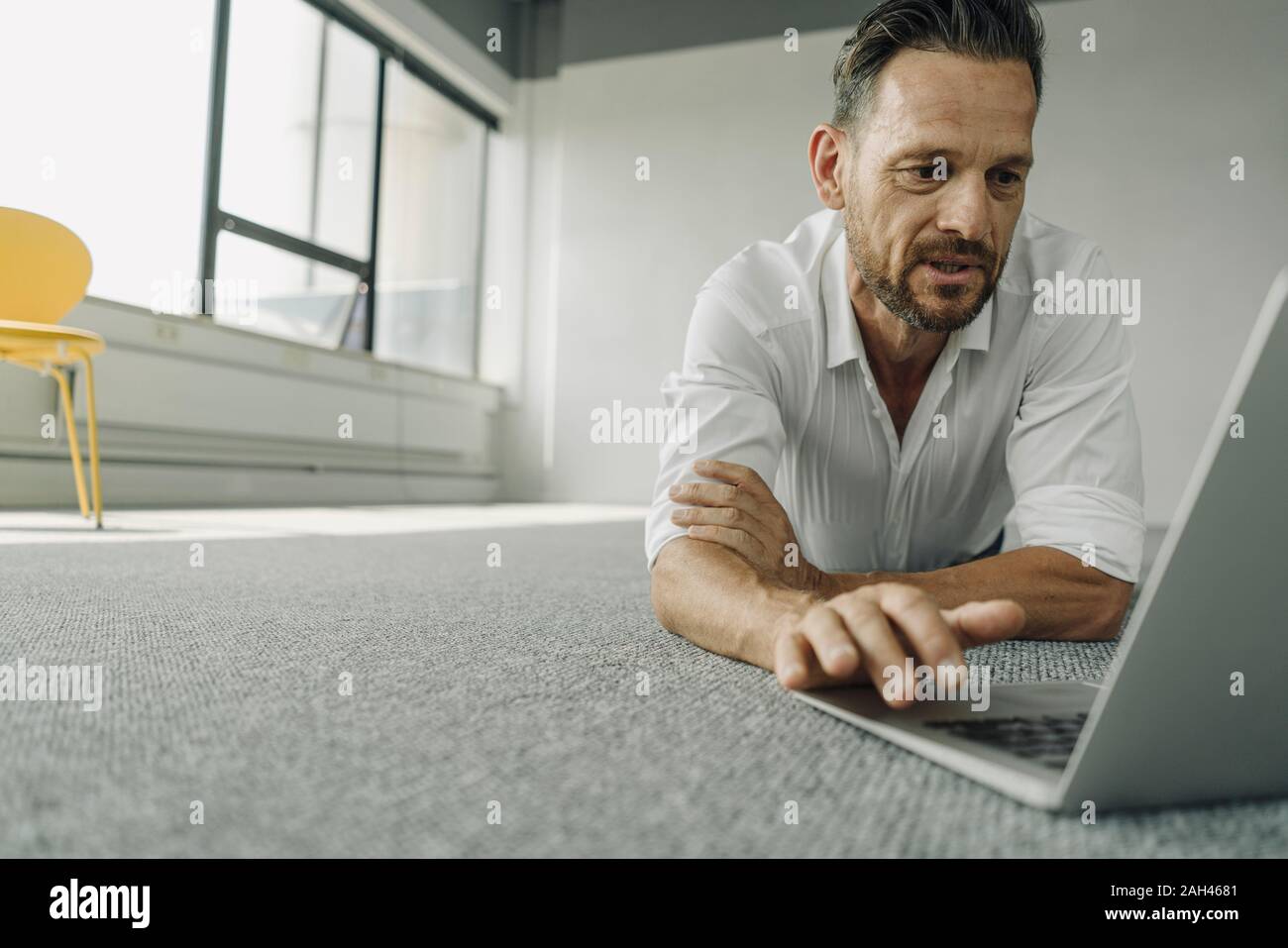Mature businessman allongée par terre dans le bureau vide using laptop Banque D'Images