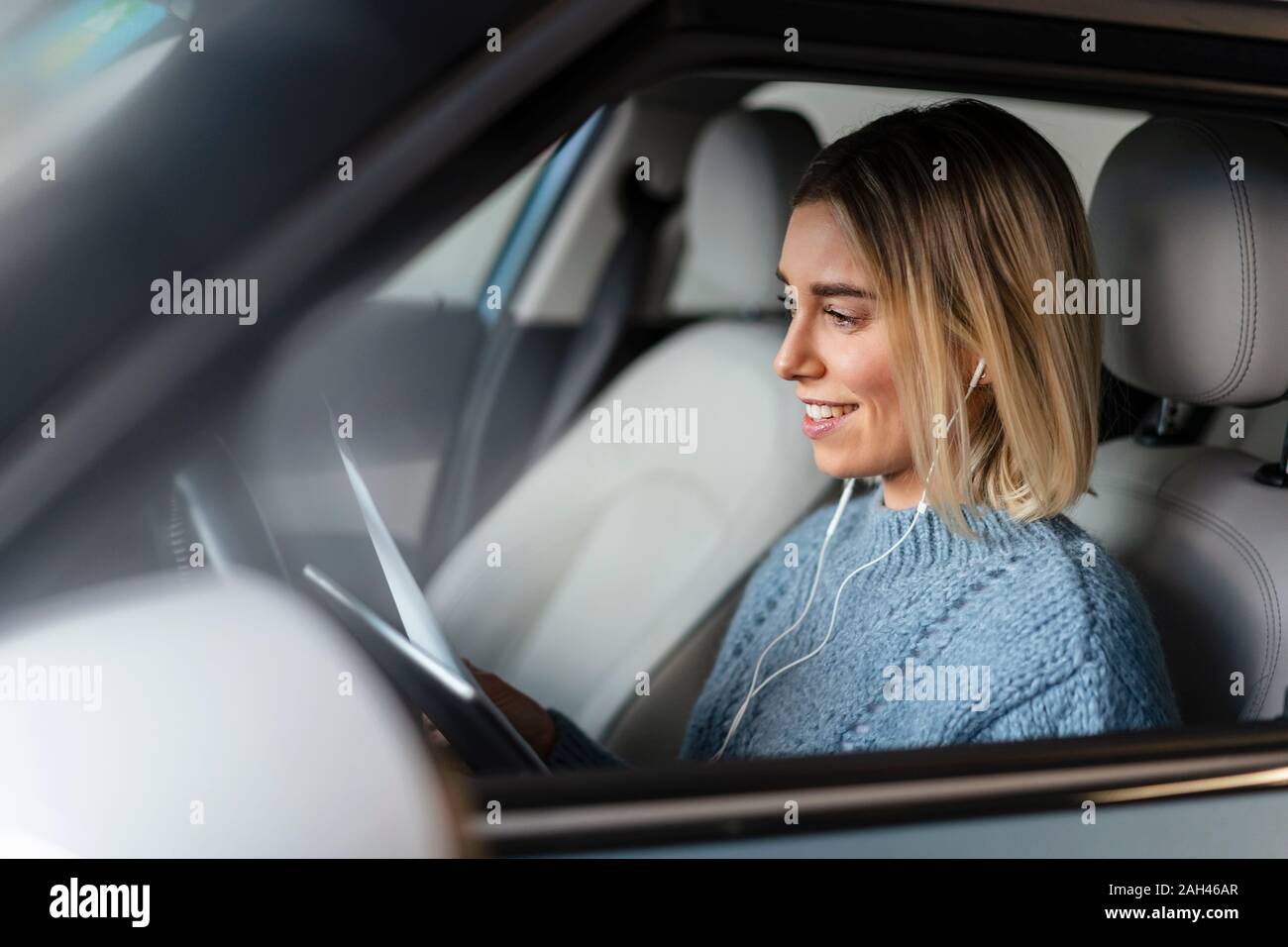 Jeune femme avec des documents, tablette et écouteurs dans une voiture Banque D'Images