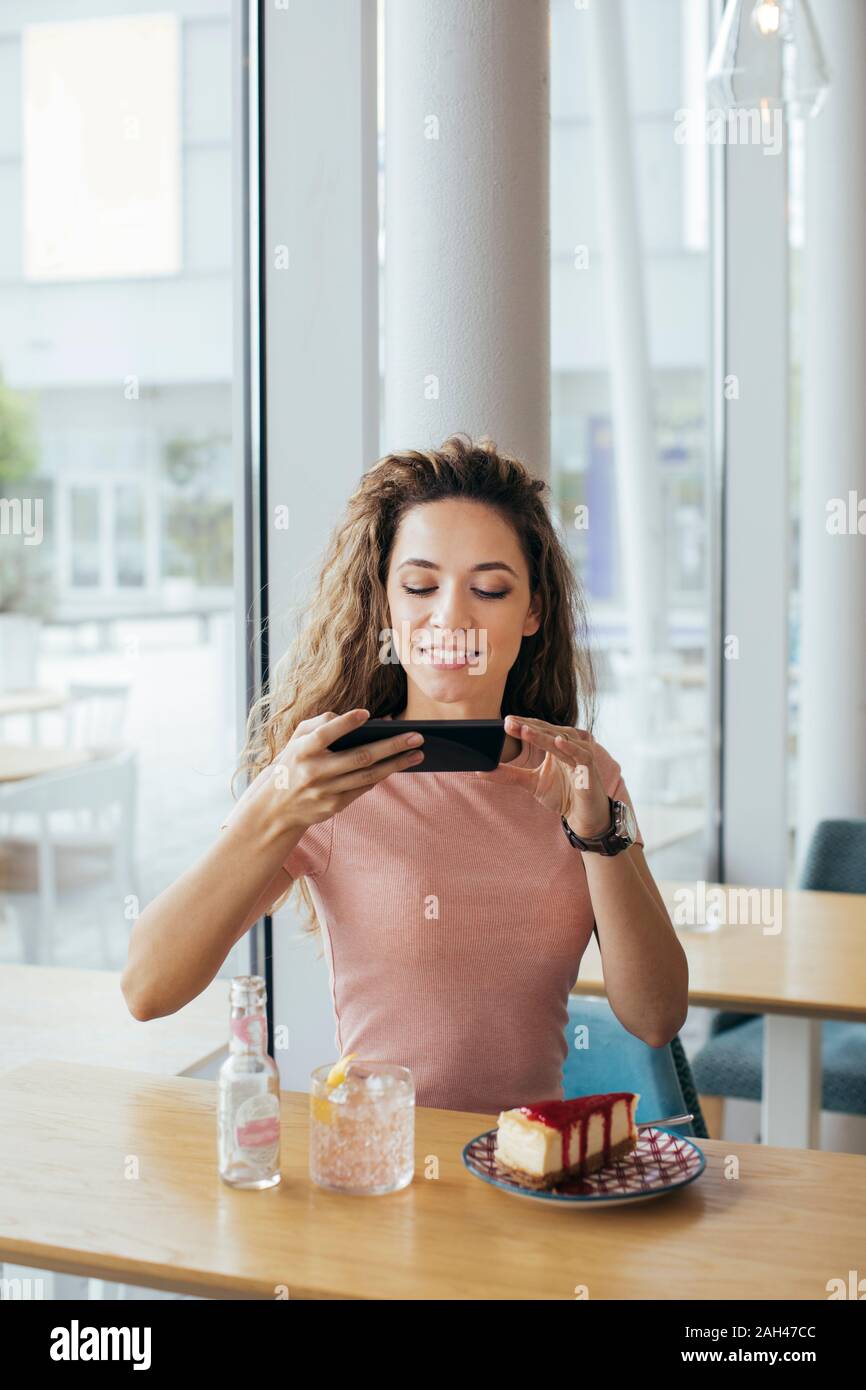 Jeune étudiant de prendre une photo de son cake at coffee shop Banque D'Images