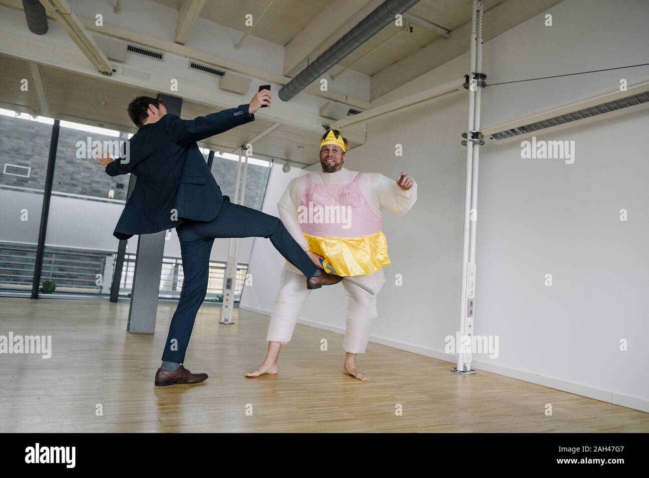 Businessman kicking man habillé en ballerine in office Banque D'Images