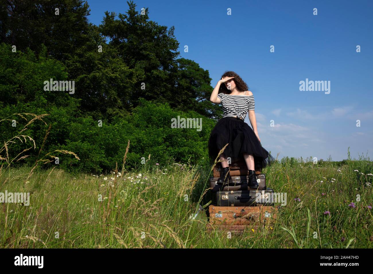 Jeune femme assise sur de vieux valises sur un pré Banque D'Images