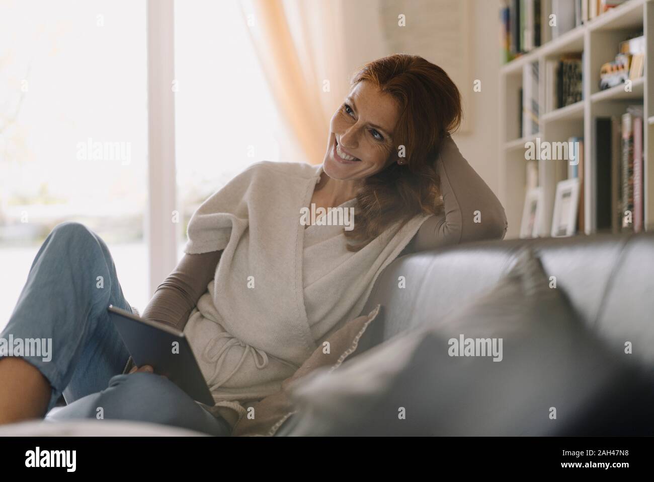 Smiling woman sitting on couch, using digital tablet Banque D'Images
