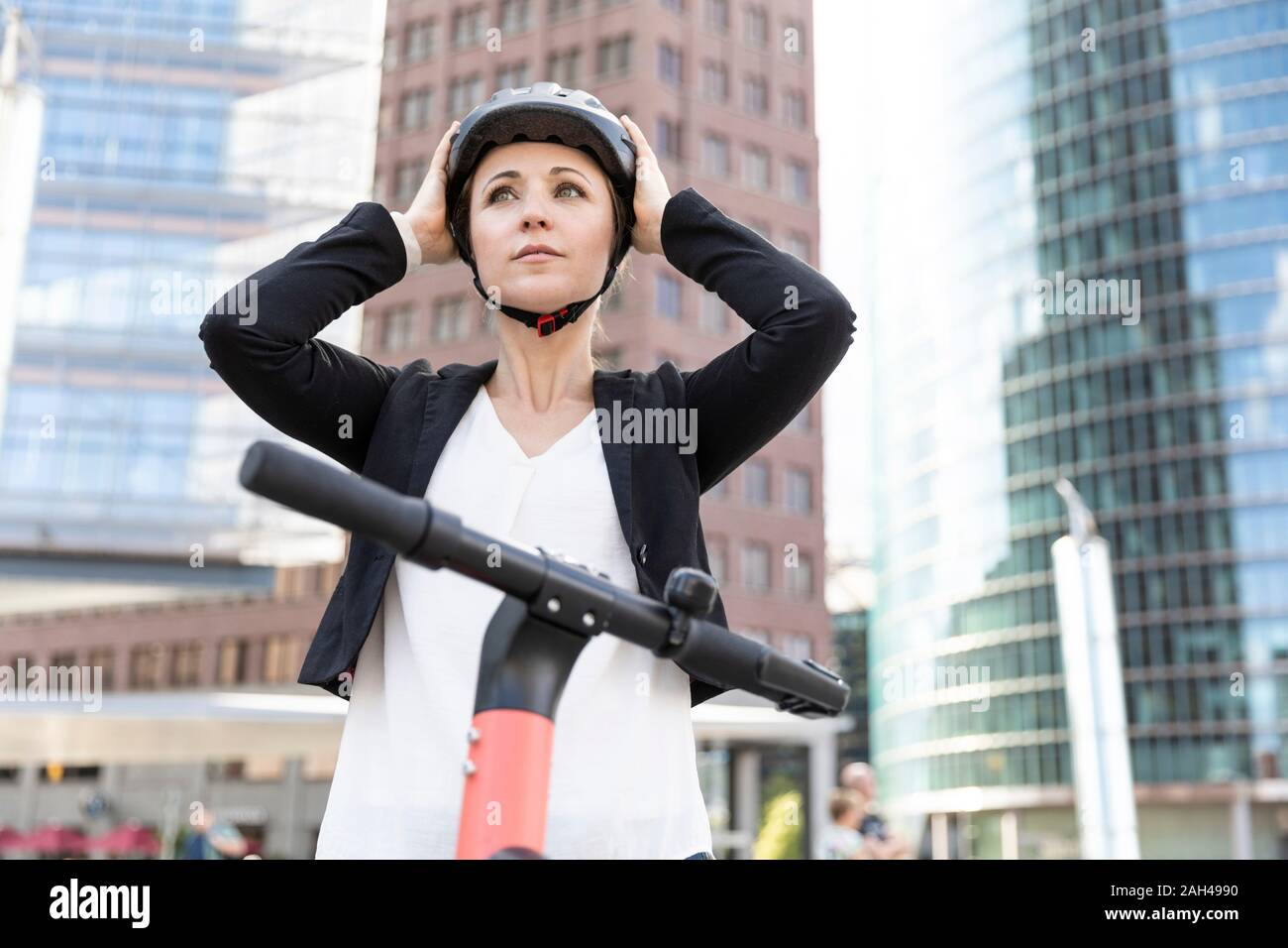 Femme avec l'e-scooter dans la ville mise sur casque, Berlin, Allemagne Banque D'Images