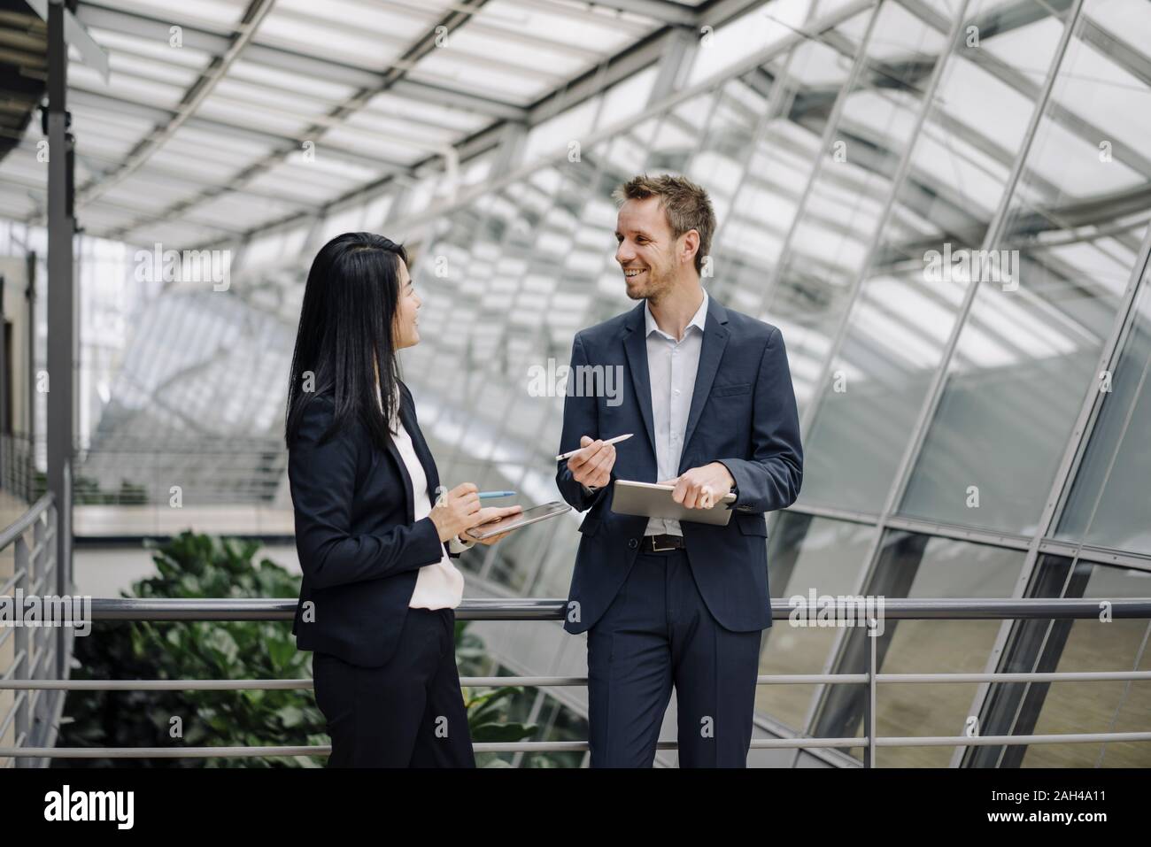 Smiling businessman and businesswoman avec les tablettes en conversation - immeuble de bureaux modernes Banque D'Images