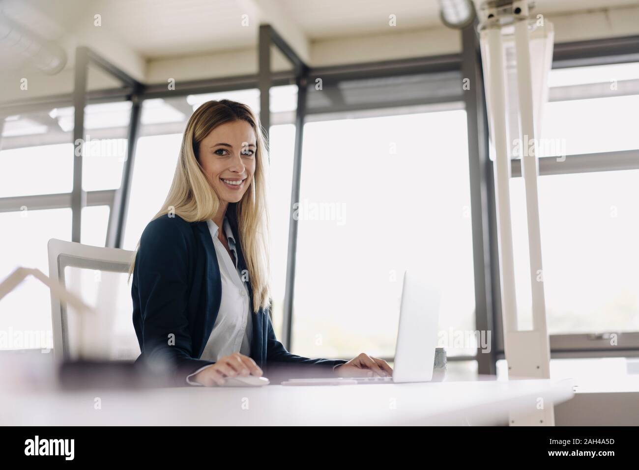 Portrait of a smiling young businesswoman using laptop at desk in office Banque D'Images