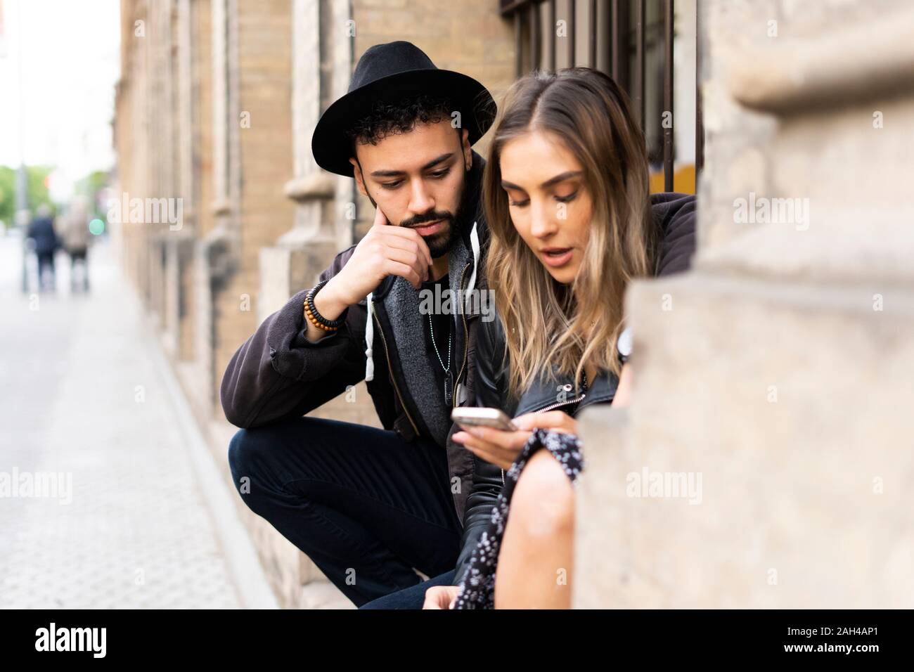 Young couple sitting outdoors looking at cell phone Banque D'Images