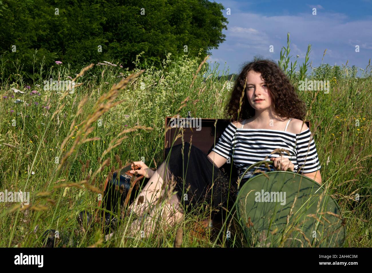 Portrait of young woman sitting in suitcase on a meadow Banque D'Images
