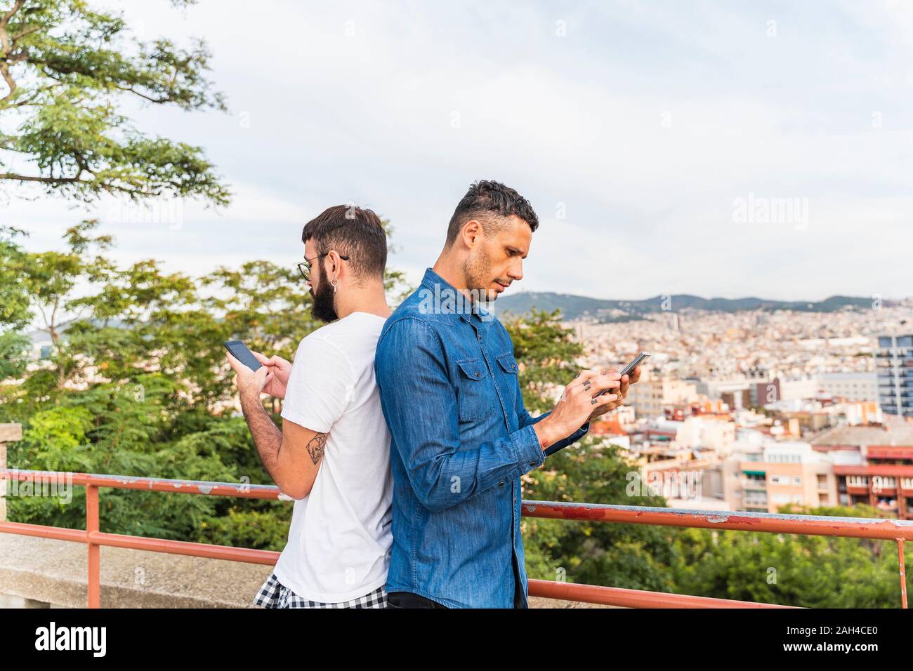 Gay couple standing back to back en utilisant les smartphones, Barcelone, Espagne Banque D'Images