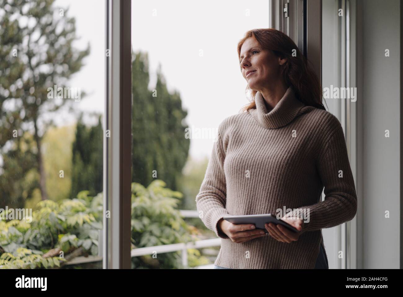 Femme à la fenêtre de sortie, holding digital tablet Banque D'Images