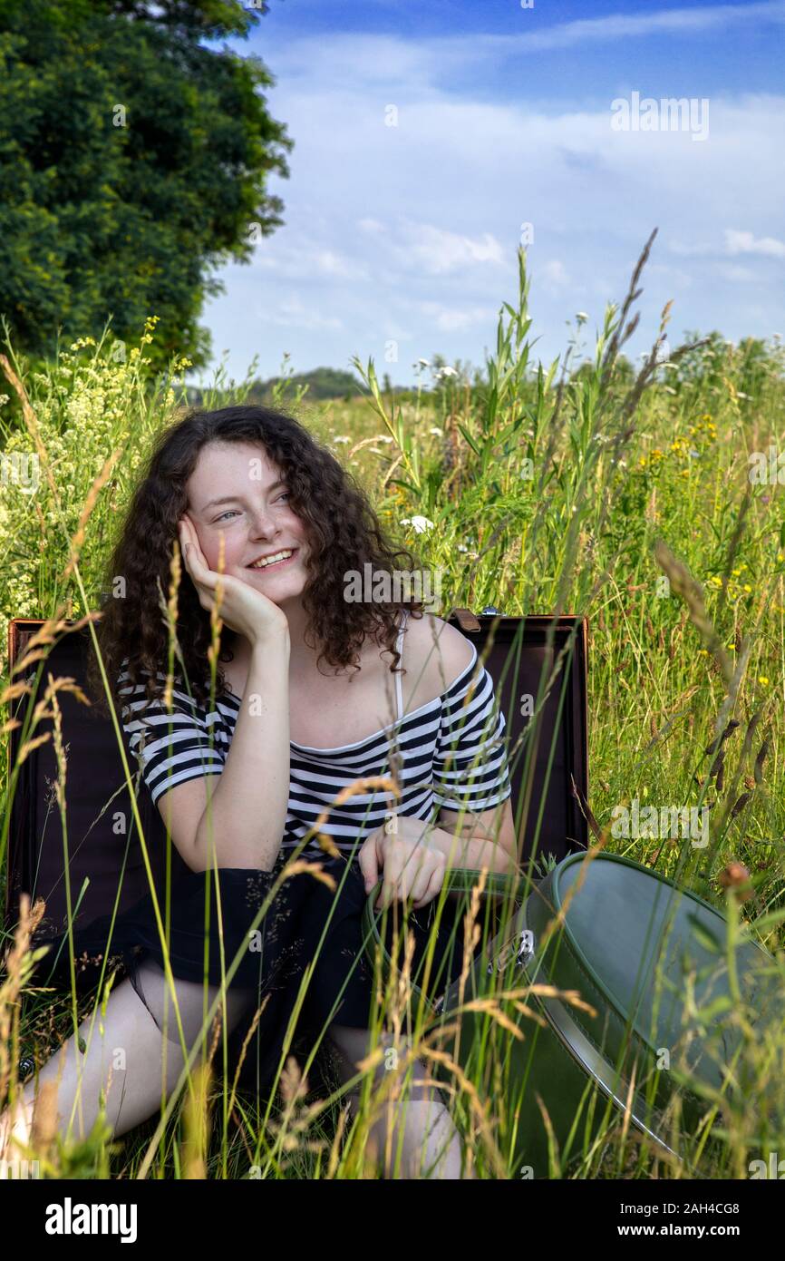 Portrait of happy young woman sitting in suitcase sur un pré à la recherche à distance Banque D'Images