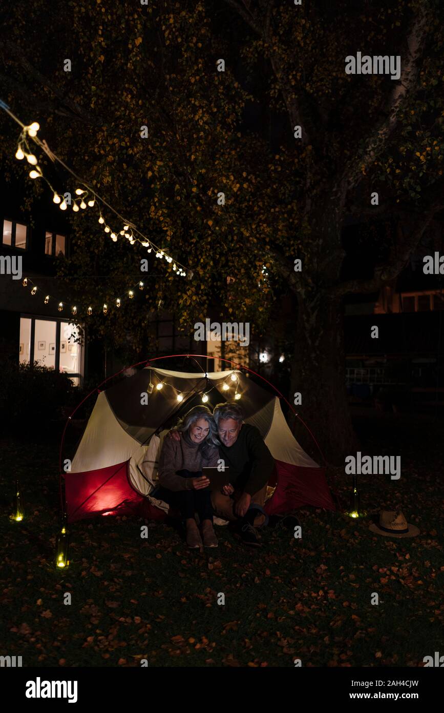 Senior couple with tablet camping dans le jardin de leur maison de nuit Banque D'Images