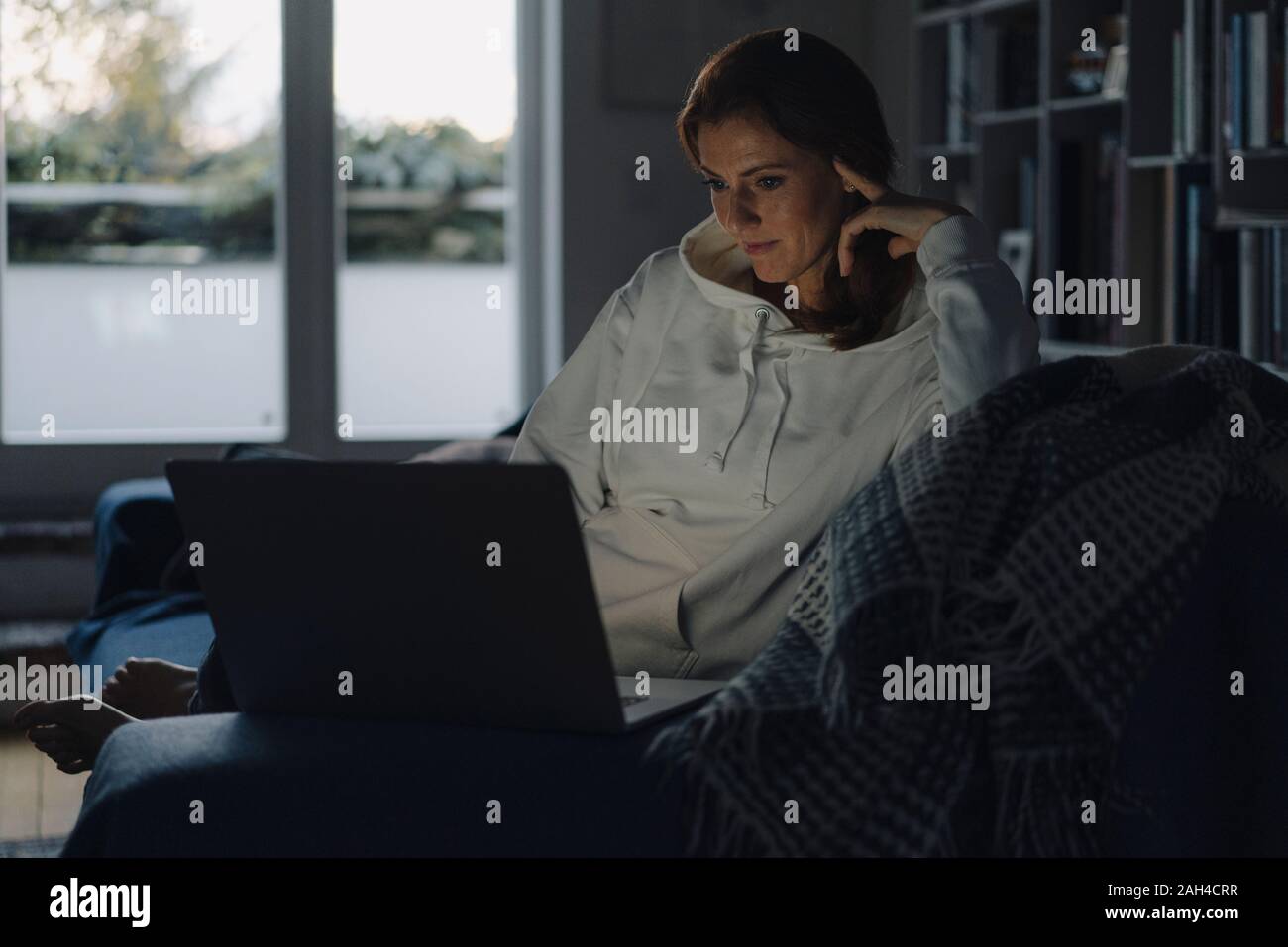 Femme assise sur la table de salon, using laptop Banque D'Images