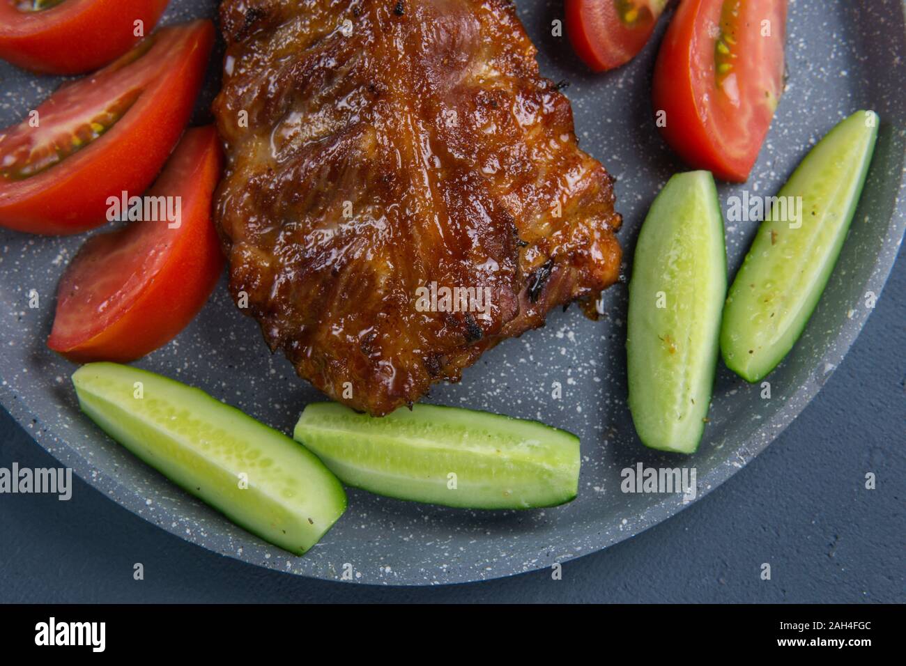 Côtes de porc au four avec du miel se coucher avec des tranches de tomates et concombres sur une table de béton gris foncé Banque D'Images