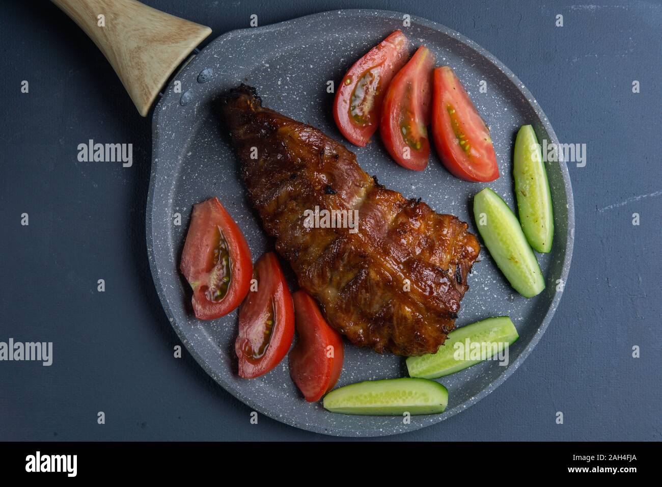 Côtes de porc au four avec du miel se coucher avec des tranches de tomates et concombres sur une table de béton gris foncé Banque D'Images