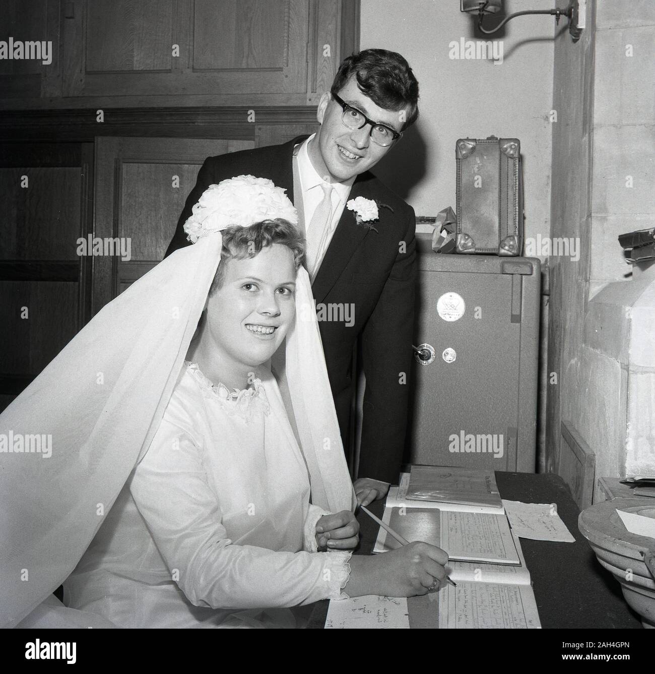 Années 1960, historiques, une femme et un homme dans une arrière-salle d'une église, avec la mariée assise, la signature du registre des mariages, England, UK. Banque D'Images