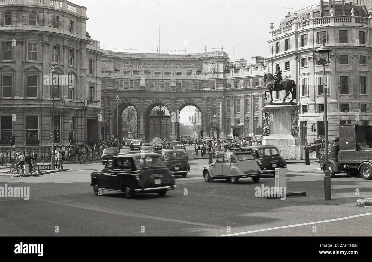 Années 1970, historiques, London Taxis et voitures de l'époque en passant par l'Admiralty Arch, Londres, Angleterre. Commandé par le roi Édouard VII pour commémorer la mort de la reine Victoria, et construit en pierre de Portland, et achevée en 1912, l'arche est un bâtiment historique qui offre un accès piétonnier et routier entre Trafalgar Square et le centre commercial, qui mène à la résidence royale, le palais de Buckingham. Banque D'Images