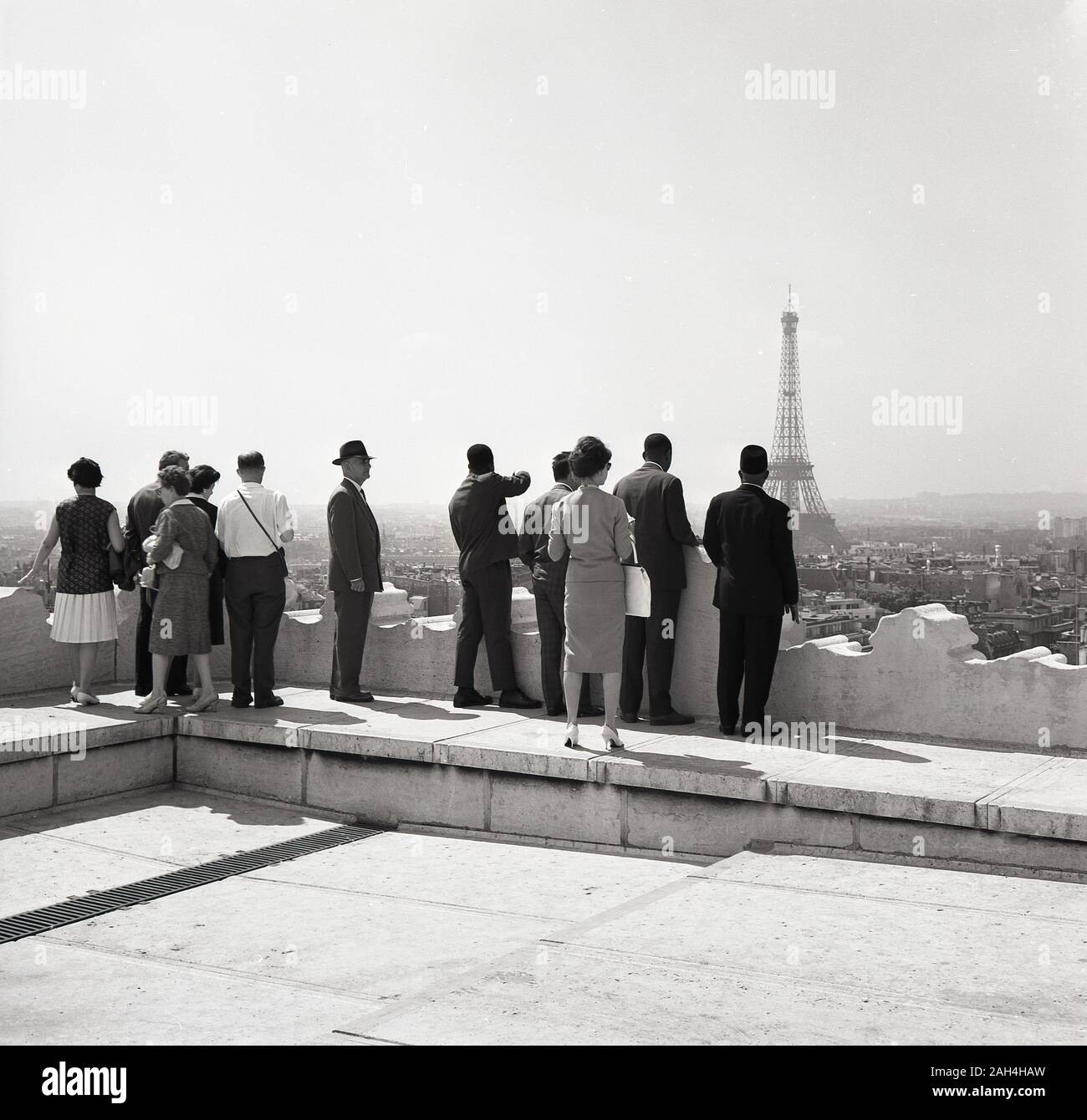 Années 1950, historiques, bien habillés les gens se tenant sur le haut d'un immeuble à la recherche sur l'horizon de la ville de Paris, la France et le célèbre monument parisien, la Tour Eiffel. Banque D'Images