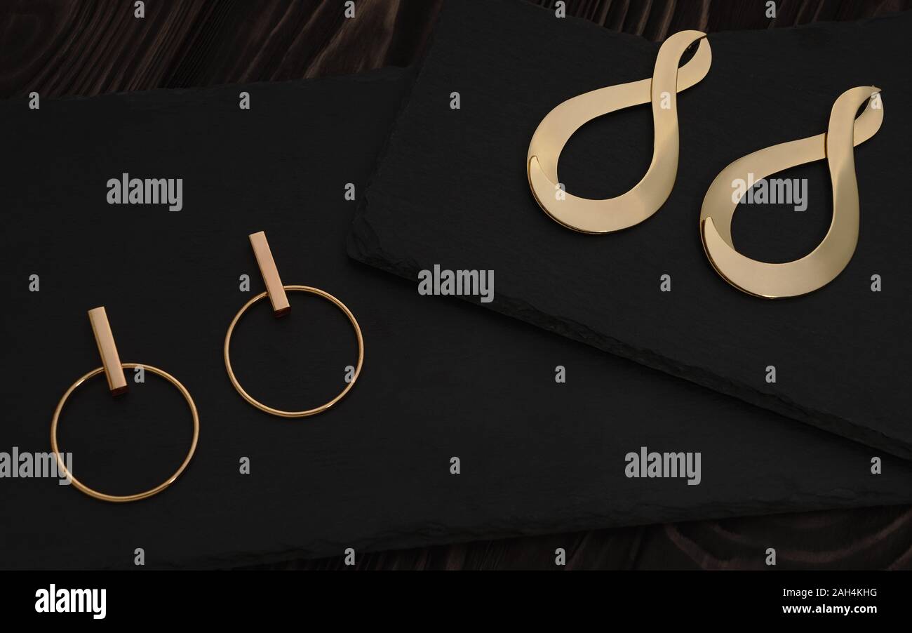 Golden Girl accessoires sur fond sombre. Paires boucles d'or moderne sur fond de pierre sombre Banque D'Images