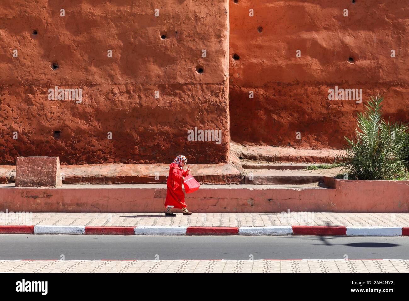 Une femme en rouge promenades le long d'un trottoir Banque D'Images