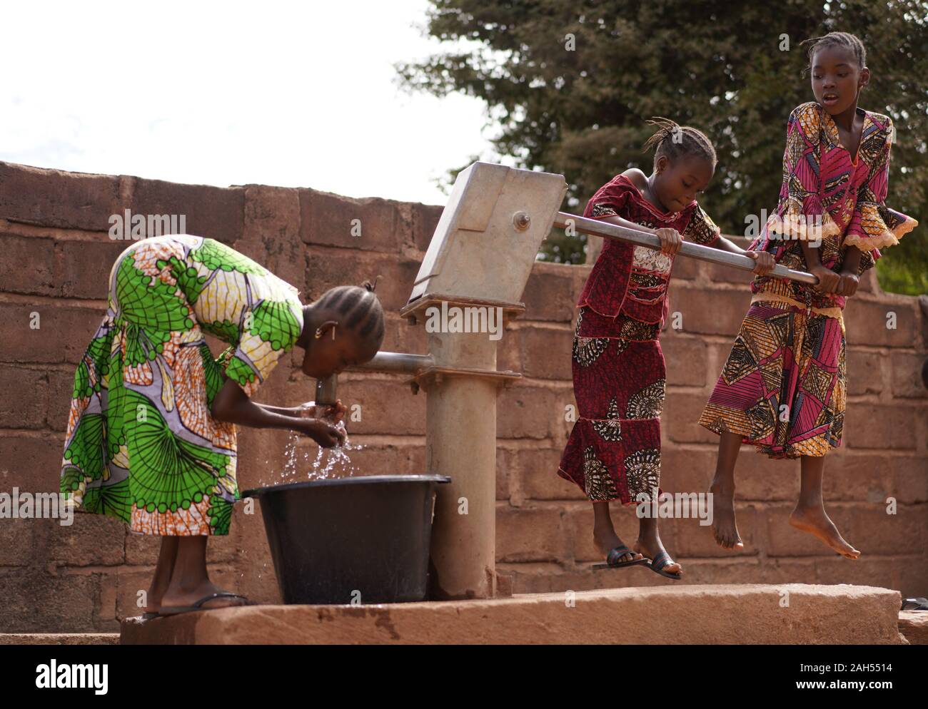 Trois Filles Africaines Qui Remplissent Des Godets À Eau À Une Pompe Publique À Trou Borgne Banque D'Images