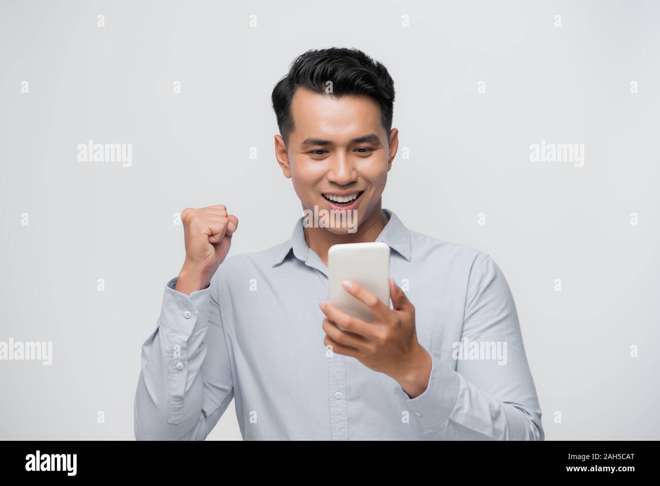 Heureux homme asiatique excité à la recherche à son smartphone et à élever son bras jusqu'à la célébration du succès Banque D'Images