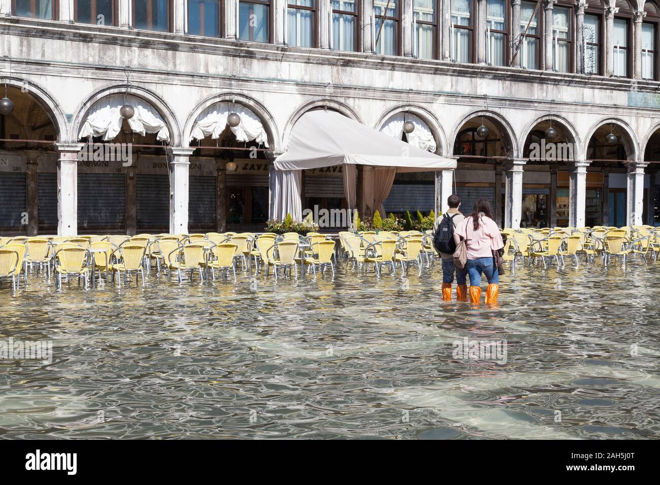 Acqua Alta inondations lors des grandes marées extrêmes de la Piazza San Marco, Venise, Italie. Les touristes regardant vide chaises de restaurant au Caffe Laverna dans l'eau d'inondation Banque D'Images