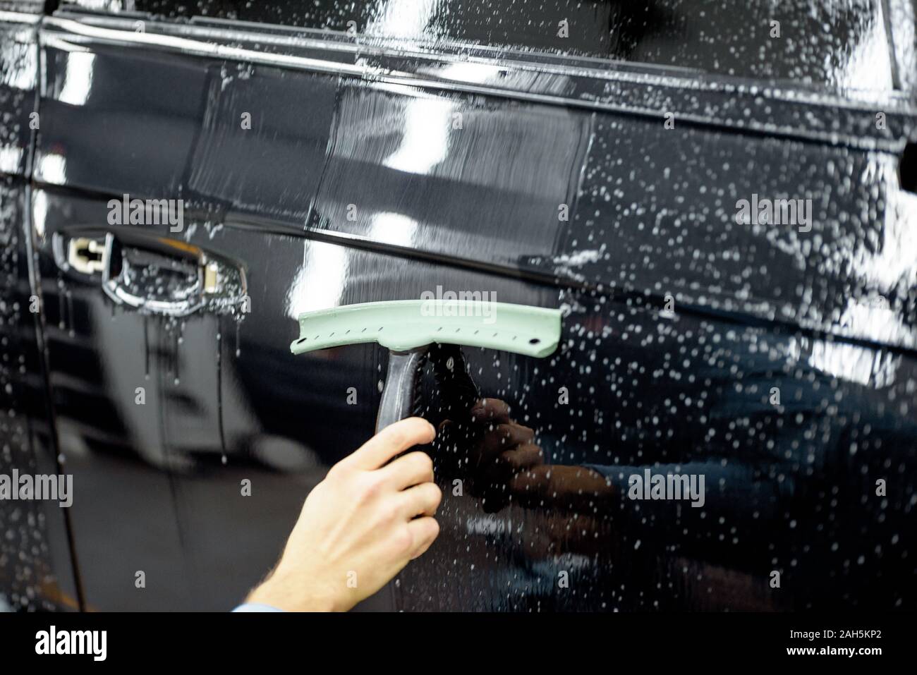 Location de la purge de l'eau du corps de voiture avec un grattoir, avant d'appliquer le film anti-gravillon au détaillant de service du véhicule Banque D'Images