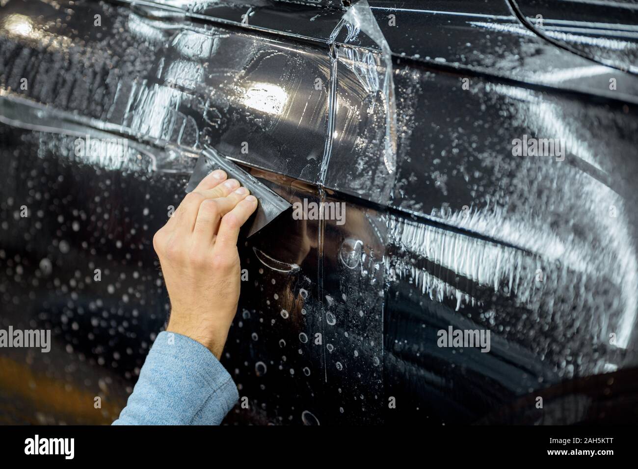 Anti-grippage travailleur film de gravier sur une voiture avec corps en détaillant les casseurs de véhicule atelier, close-up. Concept de protection de corps de voiture avec des films spéciaux Banque D'Images