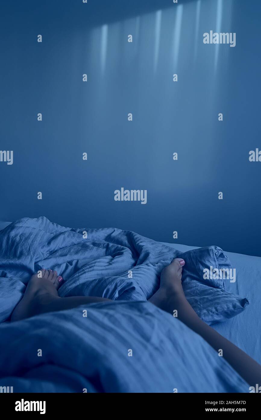 Libre les jambes des femmes sont en beige literie en chambre cosy. Matin tranquille et paresseux concept, copy space, verticale, avec des tons de couleur bleu classique Banque D'Images