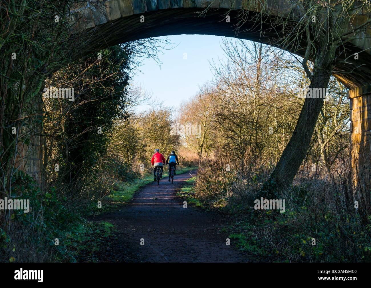 East Lothian, Ecosse, Royaume-Uni, le 25 décembre 2019. Le jour de Noël de l'exercice sur le chemin de fer à Haddington Longniddry avec un couple riding bicycles vu à travers l'arche d'un pont Banque D'Images